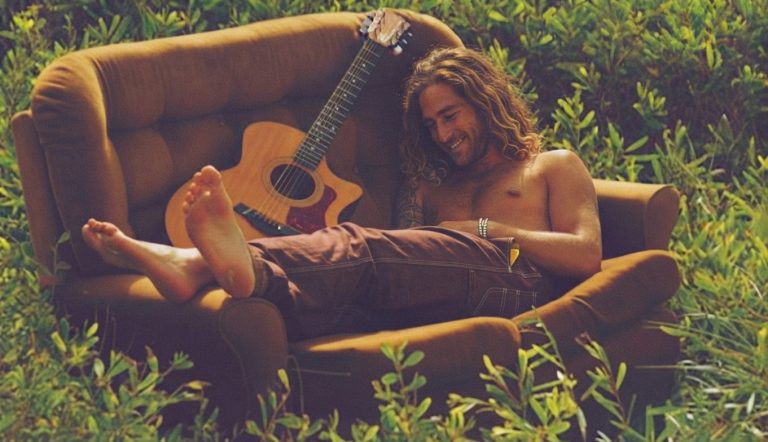 Man reclining outdoors with an acoustic guitar